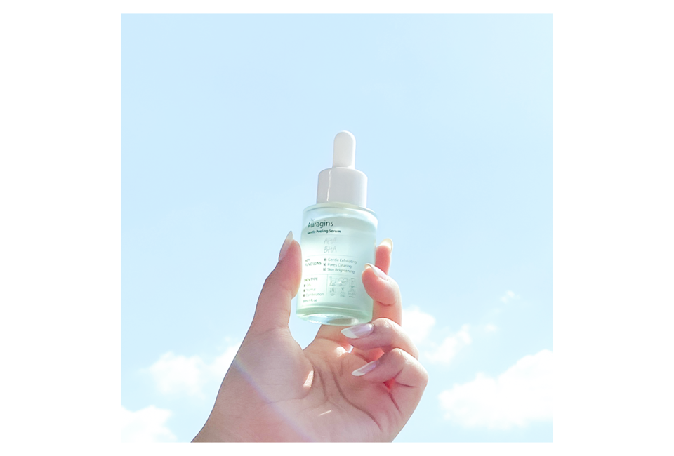Tinh chất tẩy tế bào chết The Auragins 7.5% AHA + 0.5% BHA Gentle Peeling Serum được cầm tay với thiết kế tinh tế, nổi bật giữa bầu trời sáng, giúp hỗ trợ làm sạch và làm sáng da.