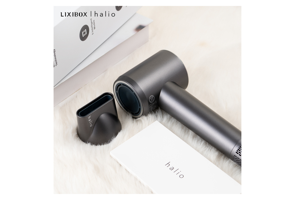 Máy Sấy Tóc Ion Âm Halio Hypersonic Hair Dryer Space Grey nằm trên nền lông trắng, đi kèm với một đầu sấy và tài liệu hướng dẫn. Thiết kế hiện đại và sang trọng, thích hợp cho việc làm tóc nhanh chóng và hiệu quả.