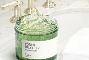 Gel Dưỡng Da Nha Đam Hương Dừa CoBa’s Daughter Aloe Soothing Gel 70gr trên bề mặt đá cẩm thạch, gần vòi nước với bánh khăn trắng, thể hiện sản phẩm chăm sóc da tự nhiên, tạo cảm giác dịu mát.
