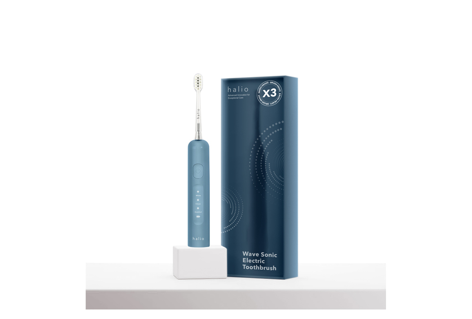 Bàn chải điện tích hợp công nghệ chuyển động kép Halio Wave Sonic Electric Toothbrush - Smoky Sky nằm trên kệ trắng cùng với hộp sản phẩm, thể hiện tính năng màu sắc và thiết kế hiện đại.